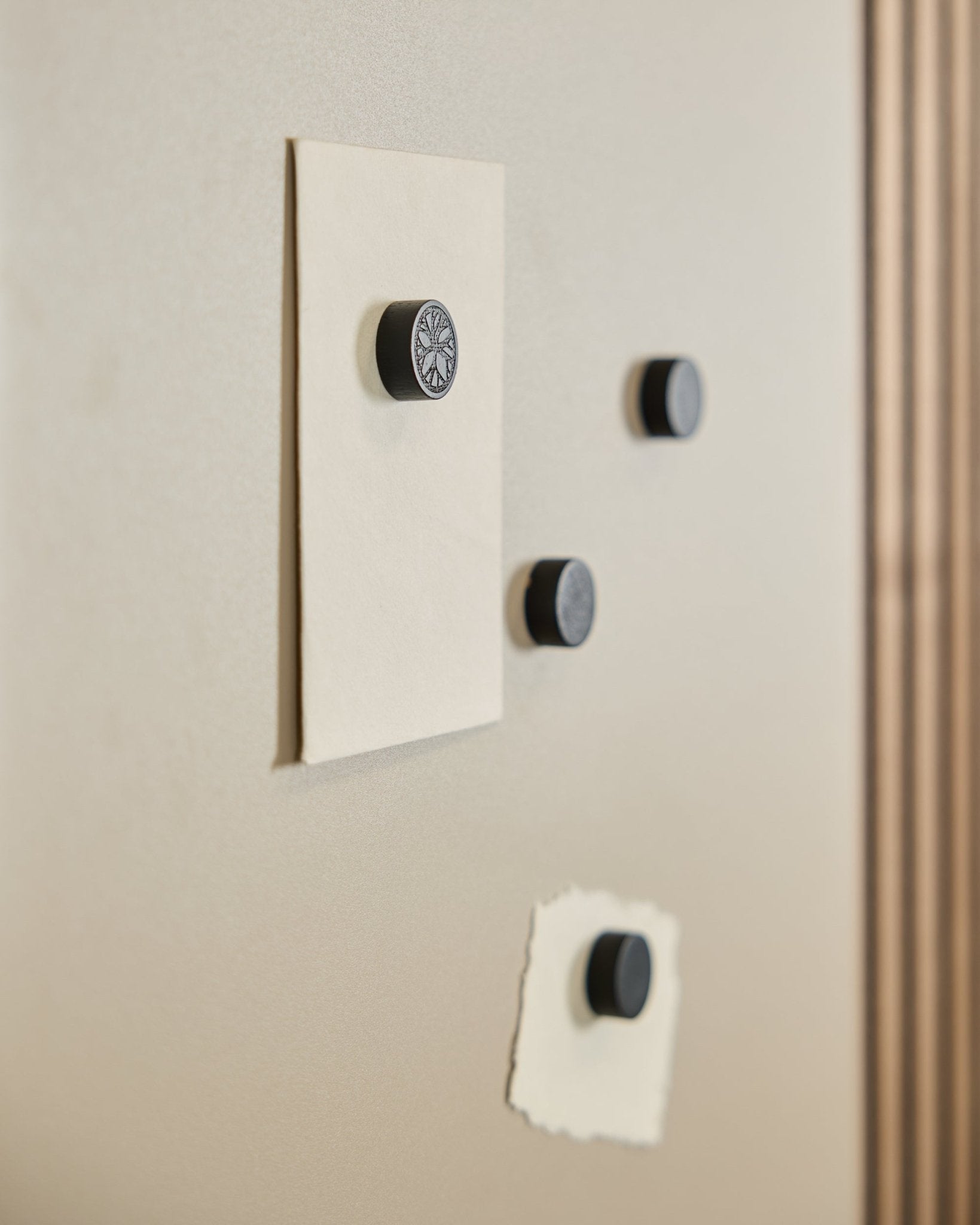 Cztery magnesy WoodUpp Norr Magnet set w kolorze Black Oak (4 szt.) podtrzymują dwie kartki na tablicy magnetycznej Norr, a po prawej stronie widoczny jest fragment Panel akustyczny.